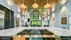 A kitchen with a large island, stainless steel appliances, and pendant lighting.