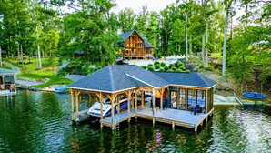 A lakeside cabin with a covered deck, dock, and boat.