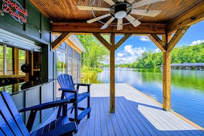 A wooden deck with Adirondack chairs, a view of a river, and a building with a neon sign.