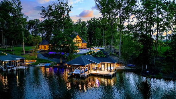 A lakeside property with multiple docked boats, a large house with a deck, and a well-maintained garden.