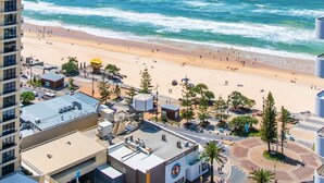 A coastal cityscape with a beach, buildings, and a surf club. - Luxury Beachfront 1BR Apt with Stunning Ocean View in the centre of Surfers (Surfers Paradise)