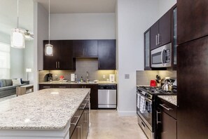 A modern kitchen with dark cabinets, stainless steel appliances, and a granite countertop island. - Peony At Millennium - Elegant 2 BDR in Houston (Houston)