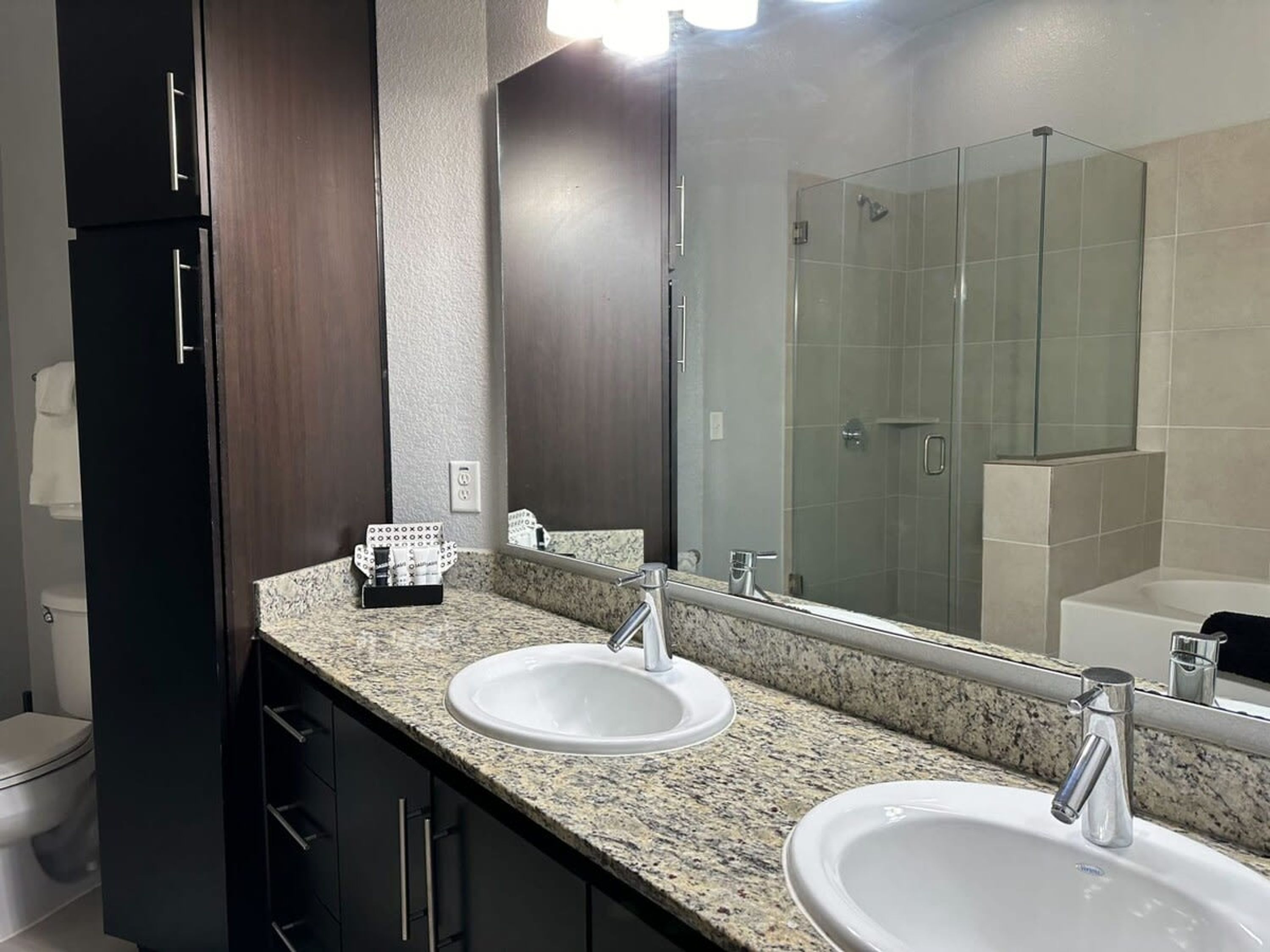 A modern bathroom with two sinks, a large mirror, and a glass shower enclosure.