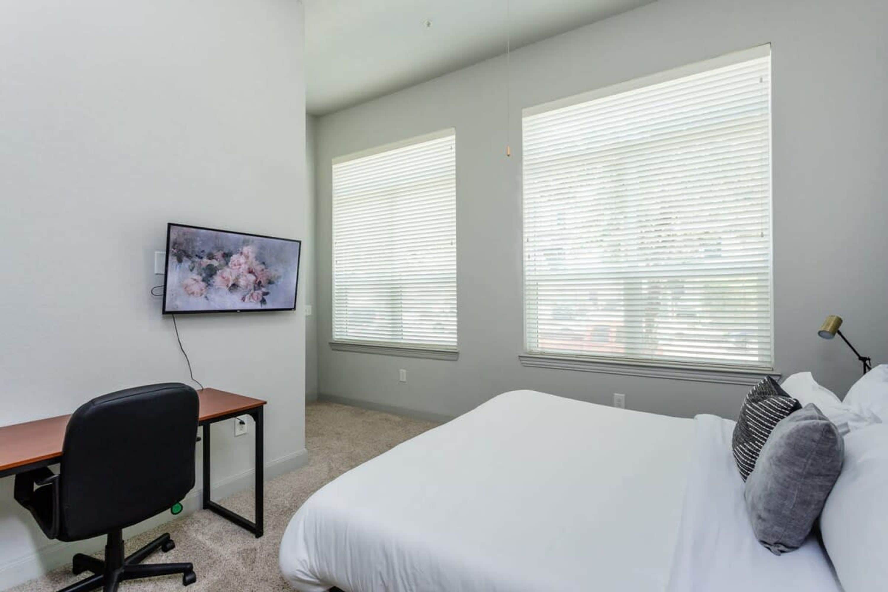 Un dormitorio con una cama, un escritorio, una silla y un televisor en la pared.