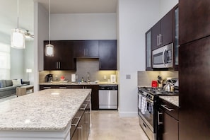 A modern kitchen with dark cabinets, stainless steel appliances, and a granite countertop island. - Peony At Millennium - Elegant 2 BDR in Houston (Houston)