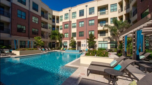A hotel with a swimming pool, lounge chairs, and a multi-story building with balconies. - Peony At Millennium - Elegant 2 BDR in Houston (Houston)