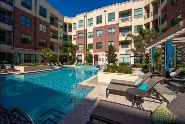 A hotel with a swimming pool, lounge chairs, and a multi-story building with balconies.