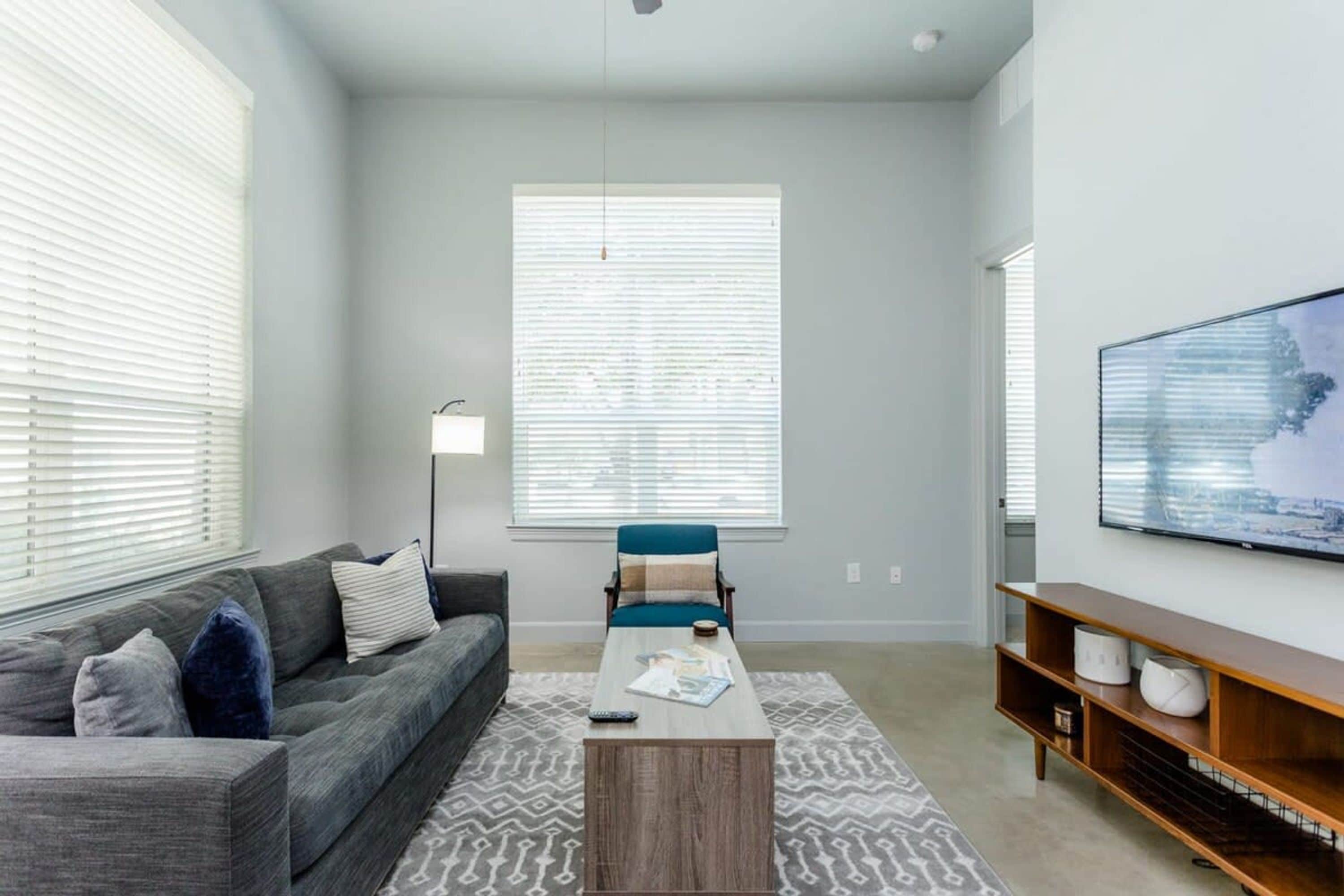 A modern living room with a grey sofa, a blue chair, a coffee table, and a TV on a wooden stand.