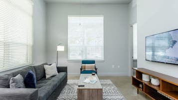 A modern living room with a grey sofa, a blue chair, a coffee table, and a TV on a wooden stand.
