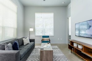 Una sala de estar moderna con un sofá gris, un sillón azul, una mesa de centro y un televisor sobre un mueble de madera.
