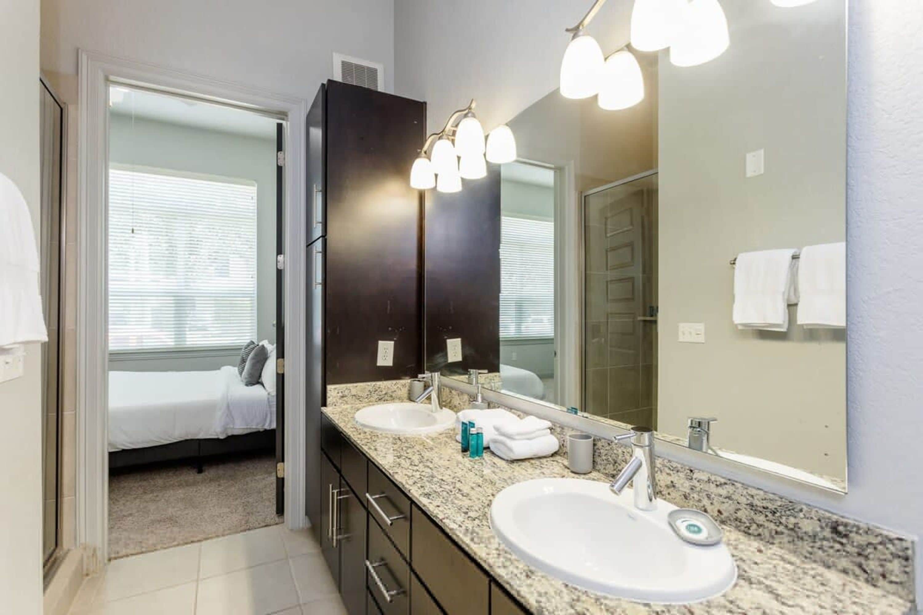 A modern bathroom with two sinks, a large mirror, and a walk-in shower.