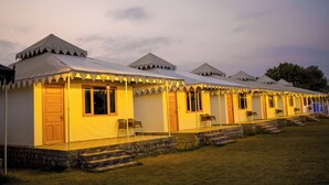 A row of white tents with wooden doors and windows, each with a small porch and steps leading up to the entrance. - Polki Farm Resort Jawai -Sumerpur (Sumerpur)
