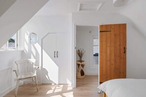 A bright, white room with a wooden door, a white chair, and a bed with a white cover. - Serene Cottage Nr the Waterfront, Topsham (Topsham)
