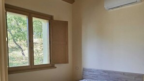 A bedroom with a wooden ceiling, a window with a view of trees, and an air conditioning unit on the wall.