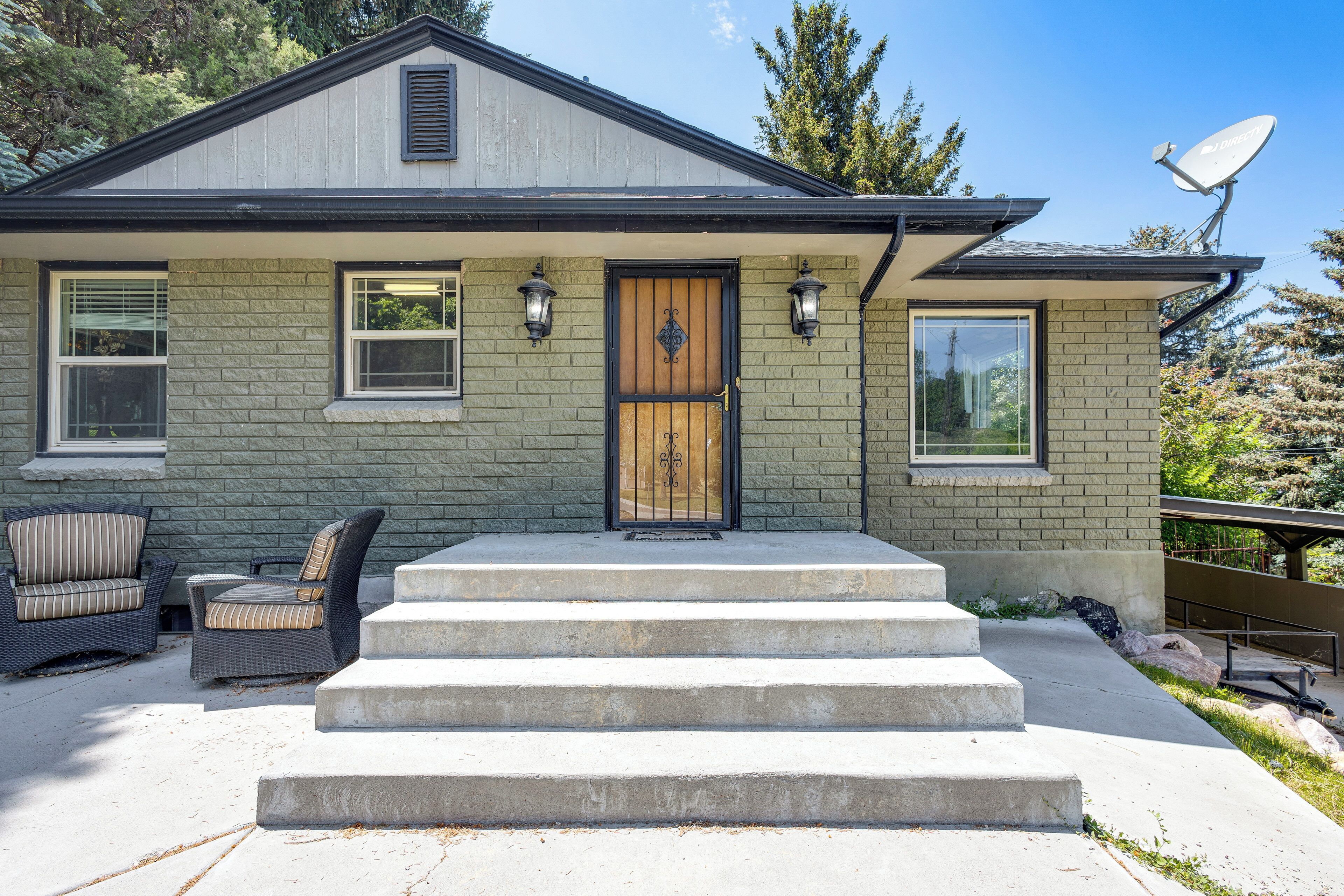 A house with a front porch, a set of steps leading to the door, and two outdoor chairs.