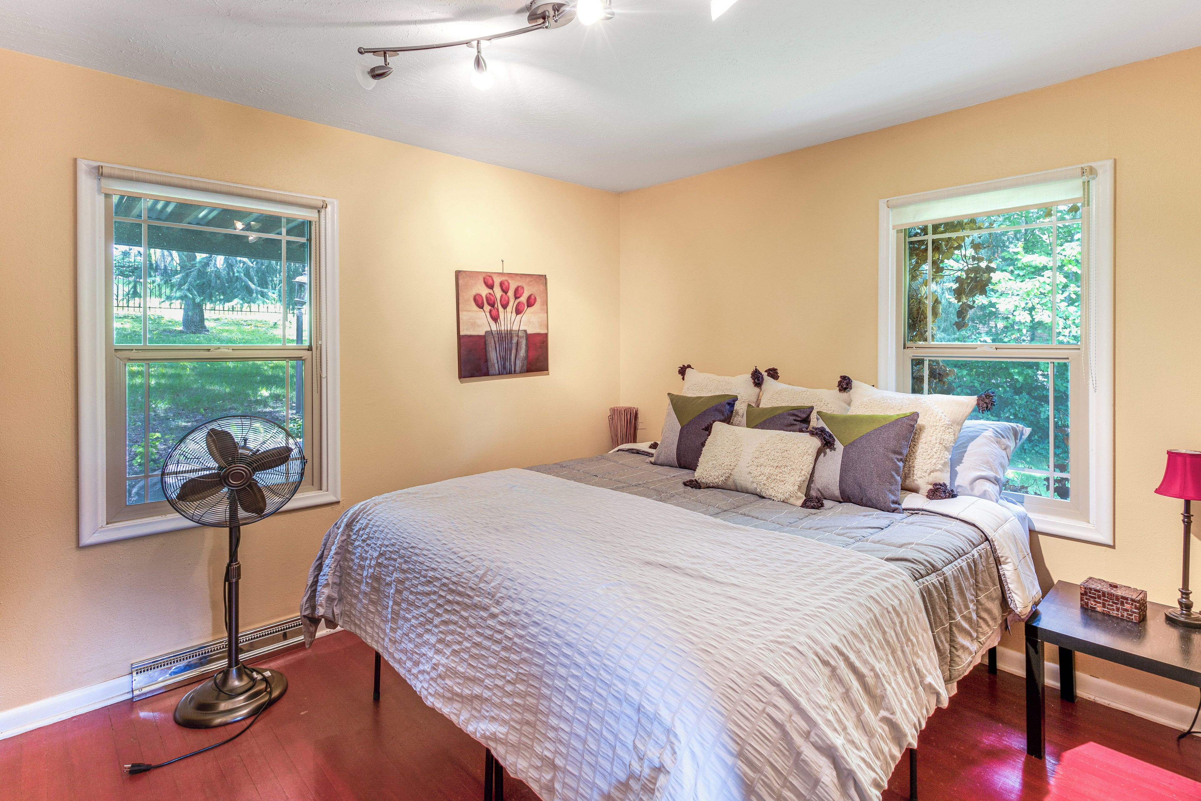 A bedroom with a bed, a standing fan, and two windows.