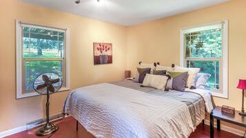 A bedroom with a bed, a standing fan, and two windows.