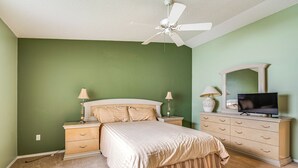 Une chambre à coucher comprenant un lit, des tables de chevet, une commode, un téléviseur et un ventilateur de plafond.