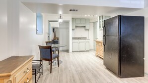 Een moderne keuken met witte kasten, een zwarte koelkast, en een eetgedeelte met een glazen tafel en stoelen.