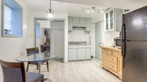 Een moderne keuken met lichte houten kastjes, een zwarte koelkast en een glazen eettafel met stoelen.