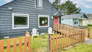 Ein zweistöckiges Haus mit Veranda, einer roten Tür und einem kleinen Tisch mit zwei Stühlen.