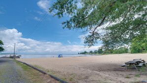 A beach with a wooden bench and a blue structure in the distance. - Fish, Relax & Enjoy Lake Views: Colonial Beach Gem (Colonial Beach)