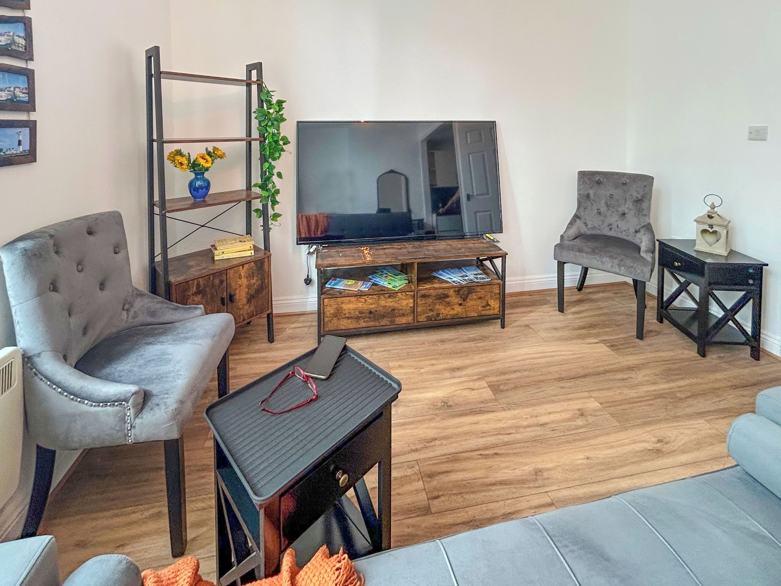 A living room with a sofa, armchair, TV stand, and a small table.
