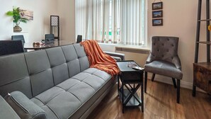 A modern living room with a grey sofa, a small table, a grey armchair, and a window with sheer curtains.