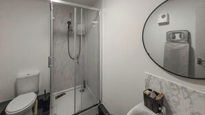 A modern bathroom with a glass-enclosed shower, a toilet, and a sink with a marble countertop.