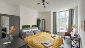 A modern hotel room with a large bed, a desk, a chair, and a window with curtains.