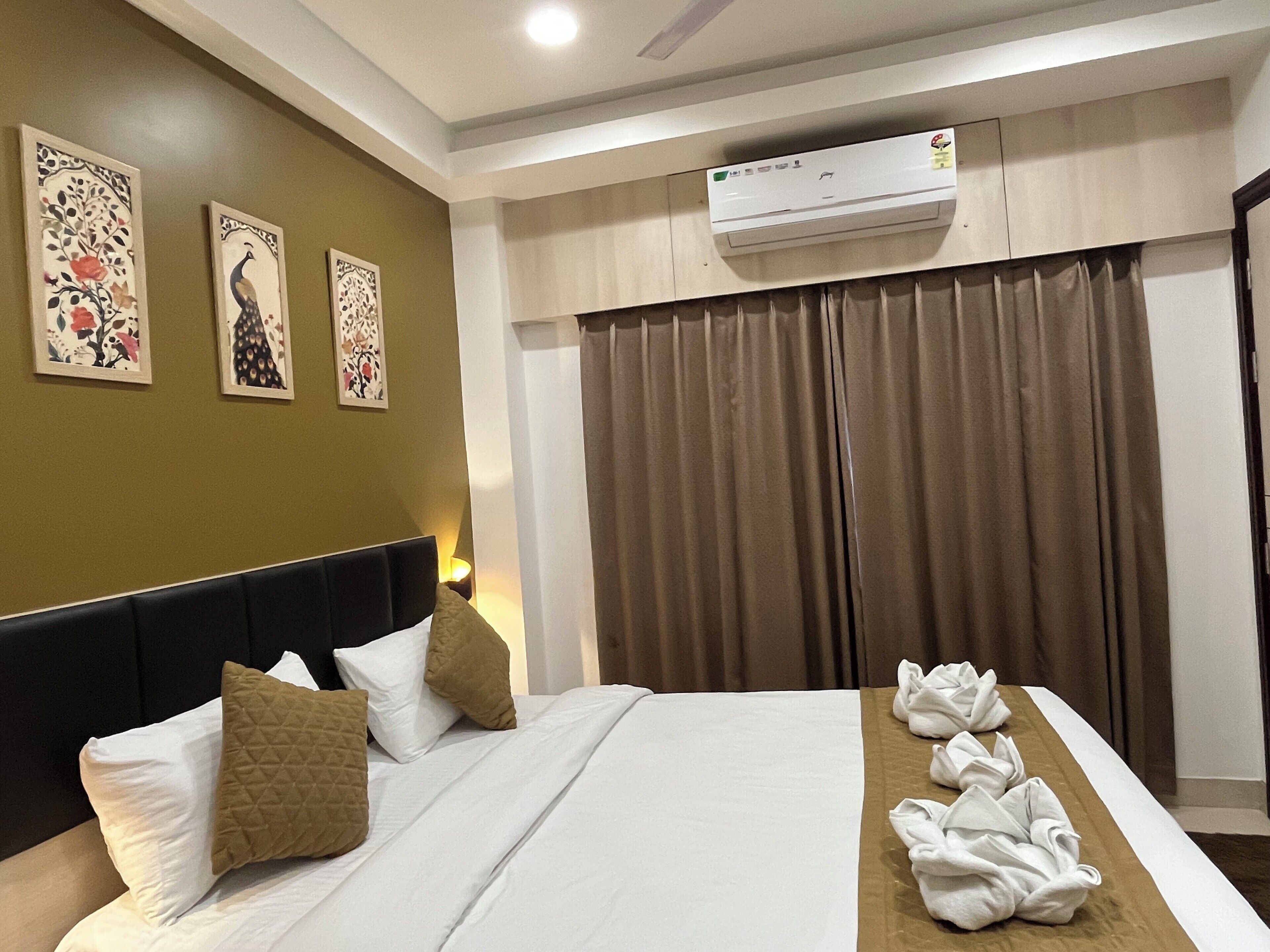 A hotel room with a bed, pillows, a wall-mounted air conditioner, and curtains.