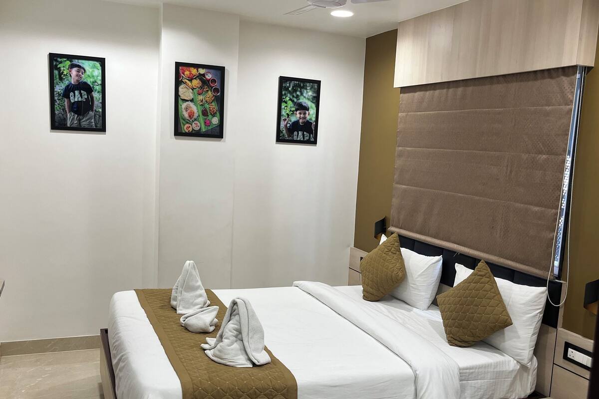 A hotel room with a bed, a headboard with a curtain, and three framed pictures on the wall.
