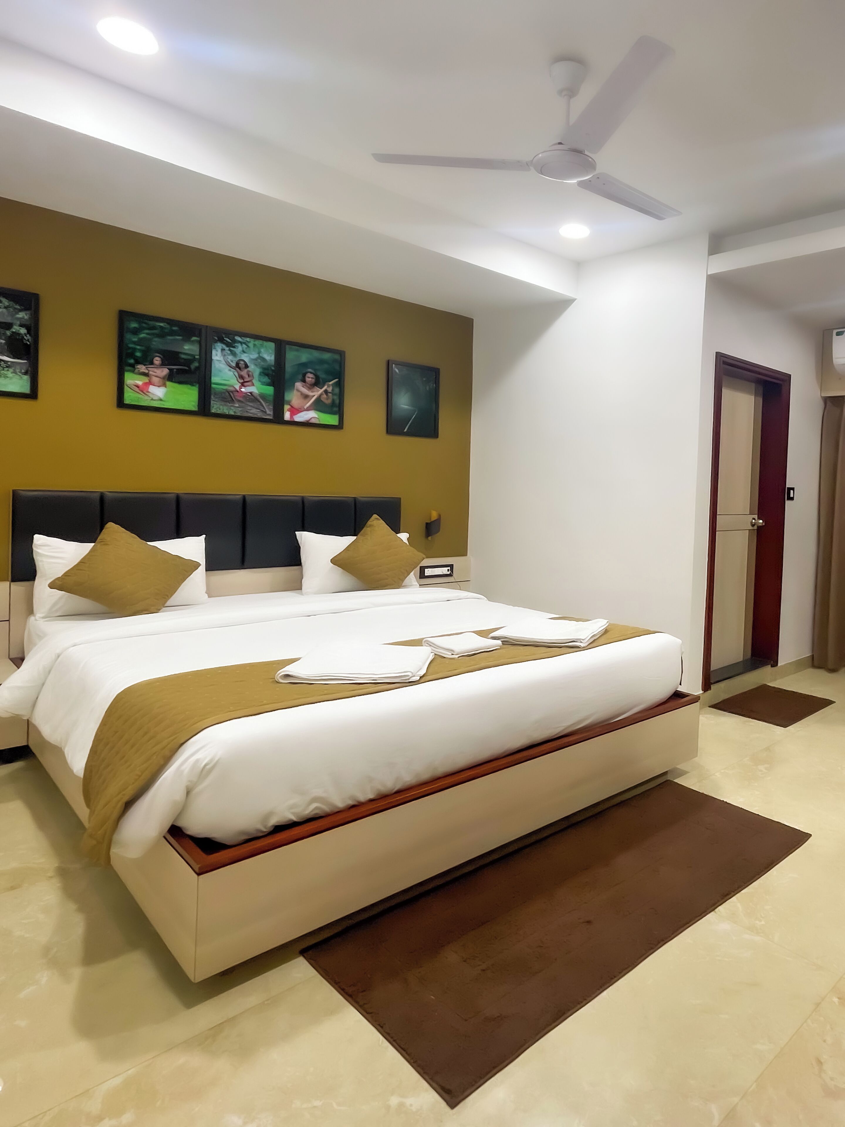 A hotel room with a large bed, a ceiling fan, and wall-mounted artwork.