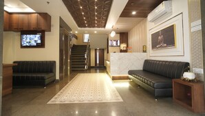 A modern lobby with a reception desk, a black leather sofa, a patterned rug, a staircase, and a framed picture on the wall. - The Executive Inn (Siliguri)