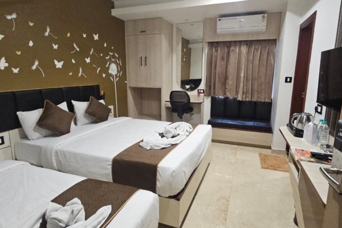 A hotel room with two beds, a desk, a TV, and a bathroom.