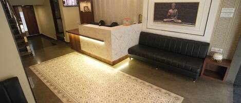 Zona de recepción de un hotel con mostrador de mármol, un sofá de cuero negro y una alfombra estampada.