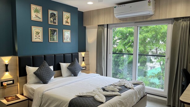 A modern bedroom with a large bed, bedside tables, wall art, an air conditioning unit, and a view of greenery through the window. - The Executive Inn (Siliguri)