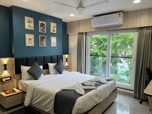Una camera da letto moderna con un letto grande, comodini, opere d'arte a parete, un condizionatore d'aria e vista sul verde dalla finestra.