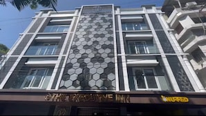 A multi-story building with a distinctive hexagonal pattern facade, a sign for 'The Executive Inn' at the ground level, and a visible air conditioning unit on the right side. - The Executive Inn (Siliguri)