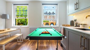 A pool table in a room with a view of a building through two windows.