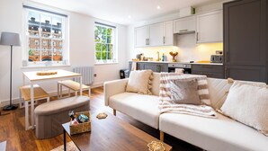A modern living room with a sofa, a dining table, and a kitchen area.