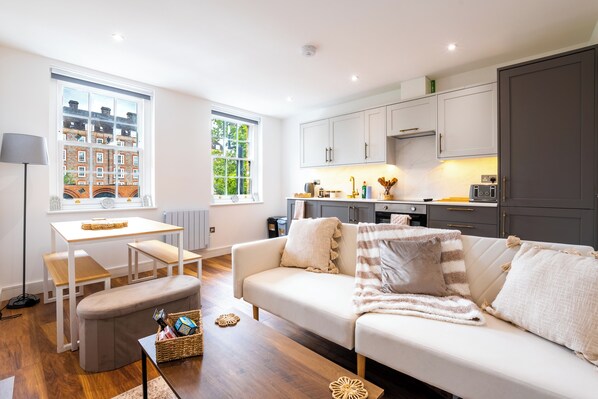 A modern living room with a sofa, a dining table, and a kitchen area.