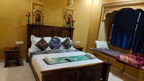 A traditional room with a wooden bed, patterned pillows, a small bedside table, and a window with a decorative frame. - Hotel Vista fort (Jaisalmer)