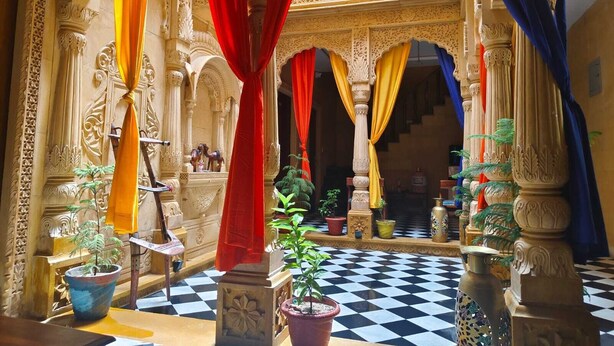 An ornate courtyard with a checkered floor, columns, and draped curtains. - Hotel Vista fort (Jaisalmer)