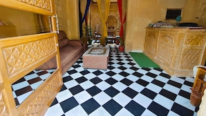 A room with a checkered floor, a sofa, a small table, and a decorative cabinet. - Hotel Vista fort (Jaisalmer)