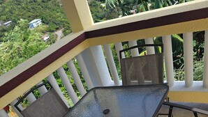 A balcony with a glass table and four chairs, surrounded by a white railing and greenery. - Baecation Romantic Getaway Couples & Singles (St. Thomas)