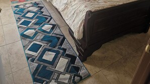 A bedroom with a bed, pillows, a patterned rug, a door with a stained glass window, and a curtain with a tropical scene. - Baecation Romantic Getaway Couples & Singles (St. Thomas)