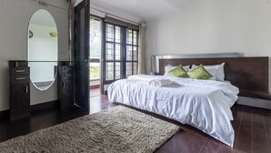 A bedroom with a large bed, a wooden headboard, a mirror, a wardrobe, and a view of the outdoors through a window. - The Whispering Pines (Mussoorie)