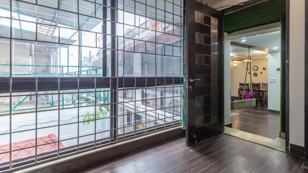 A room with a large window, wooden flooring, and a door leading to another area. - The Whispering Pines (Mussoorie)