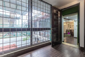 A room with a large window, wooden flooring, and a door leading to another area. - The Whispering Pines (Mussoorie)
